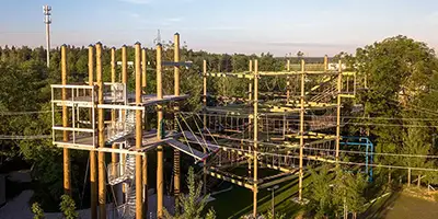 Großes Bauwerk aus Holz, Metall und Seilen. Links sind mehrere Plattformen in unterschiedlicher Höhe, die durch Säulen gestützt werden. Im rechten Bereich sind über mehrere Ebenen verschiedene Hindernisse aus Seilen und Holz aufgebaut. Bild zur Verfügung gestellt von Jochen Schweizer Arena GmbH, München