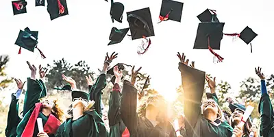 Viele Studenten im schwarzen Talar, die ihre Absolventenhüte in die Luft werfen.
